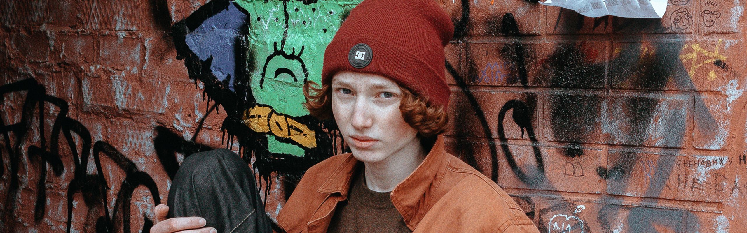 Boy wearing a hat sitting against a graffiti wall