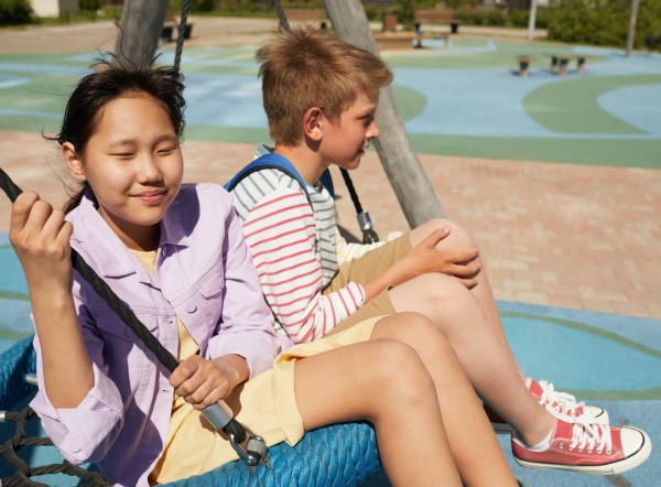 Two children sitting on a swing in a playground